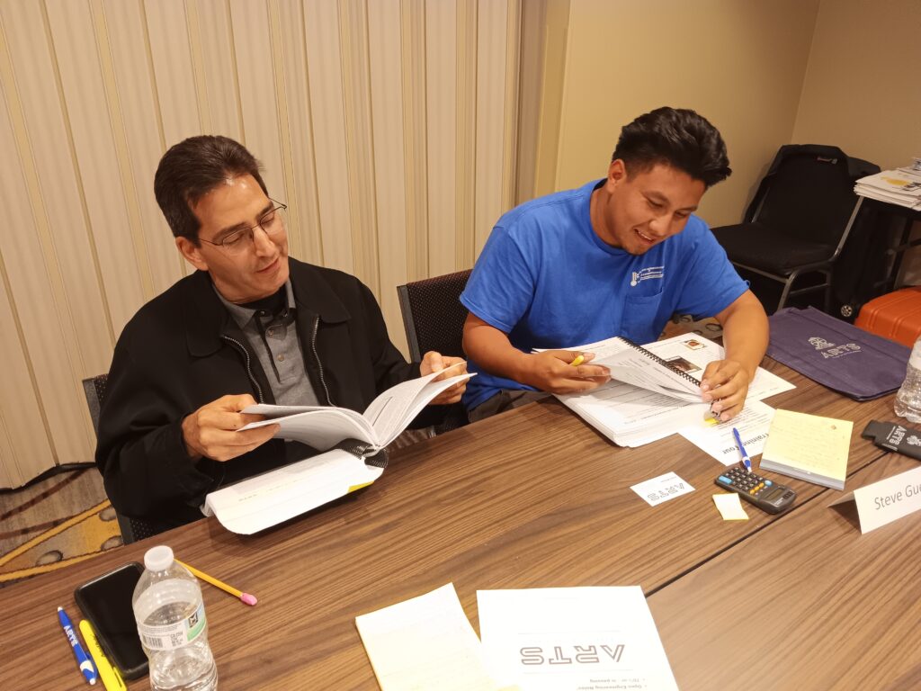 Two men sitting at a table with papers and pens.