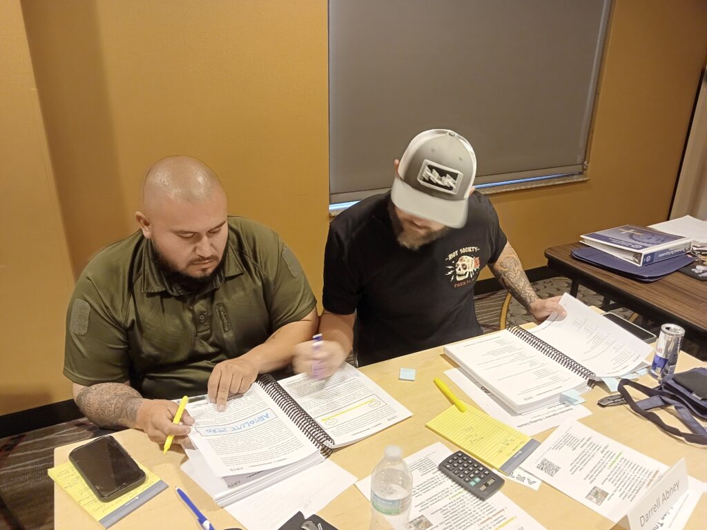 Two men sitting at a table with papers and pens.