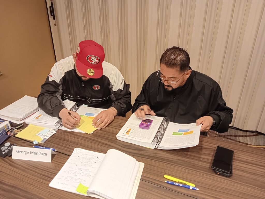Two men sitting at a table with papers and pens.