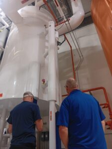 Two men in blue shirts are standing next to a large white tank.