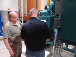Two men are looking at a machine in the room.