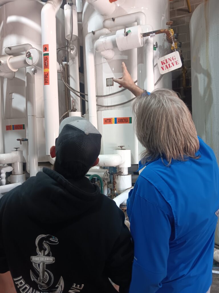 Two people are looking at a sign in front of pipes.