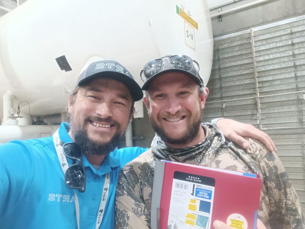 Two men are posing for a picture in front of an airplane.