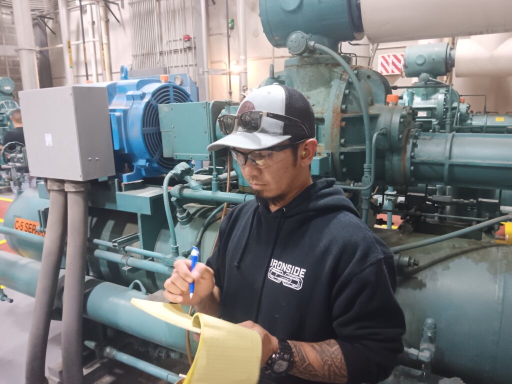 A man writing on paper in front of an industrial machine.