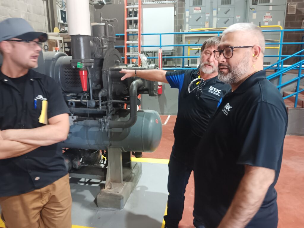 A group of people standing around looking at some pipes.