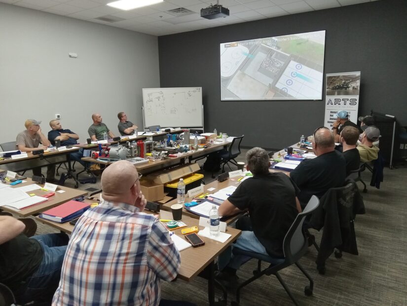 A group of people sitting at tables in front of a projector screen.