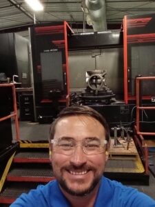 A man in glasses and safety goggles smiling for the camera.