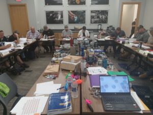 A group of people sitting around tables with papers on them.