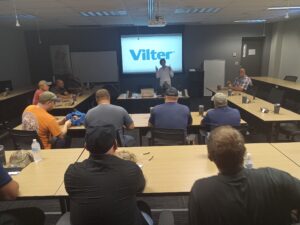 A group of people sitting at tables in front of a projector screen.