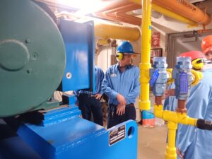 A man in blue shirt and hard hat next to pipe.